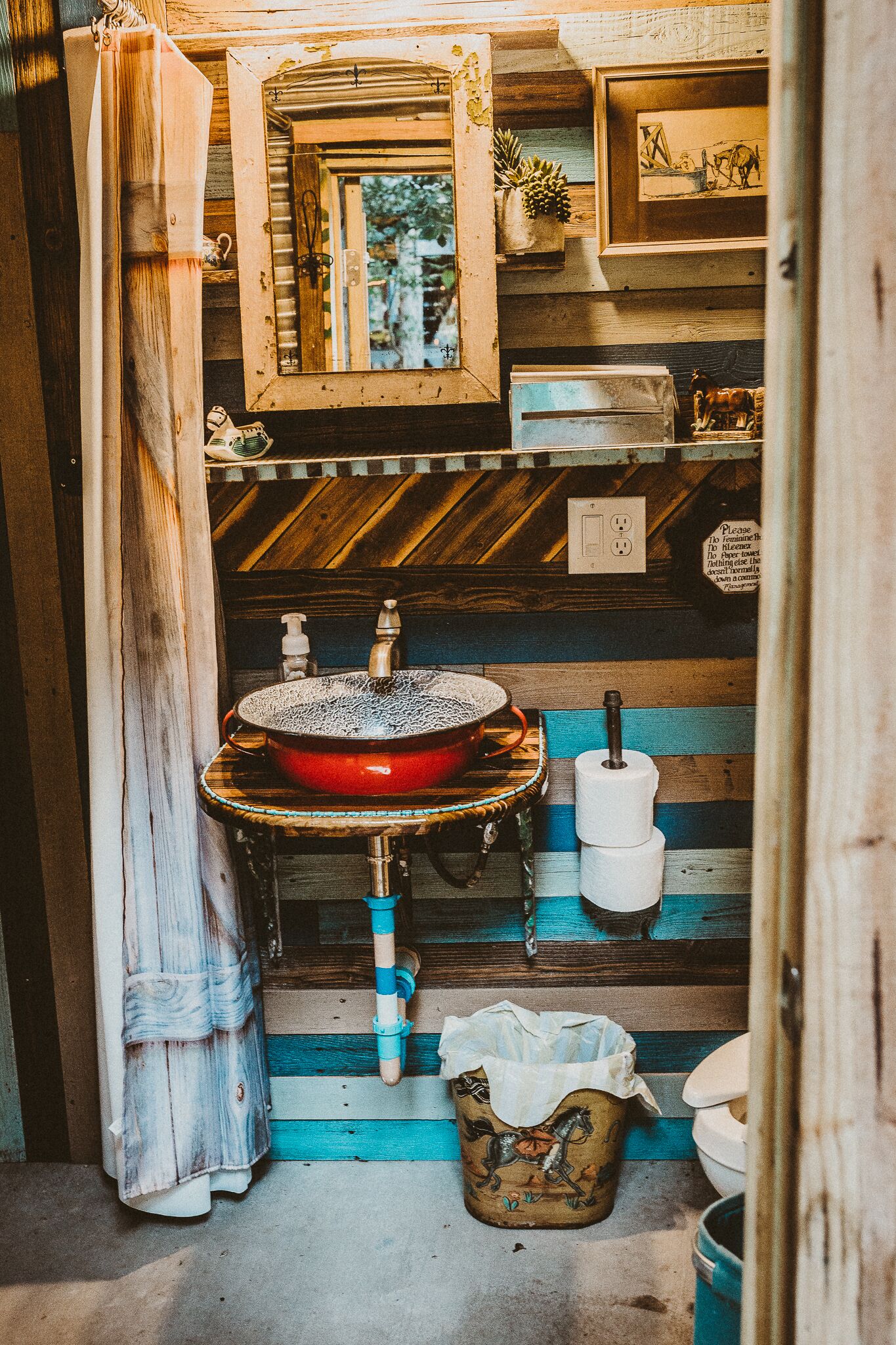 A rustic bathroom with a wooden interior, a red sink, a mirror, and a small shelf with decorative items.