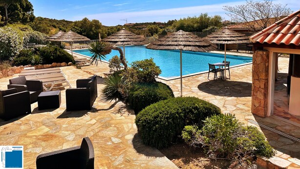 A pool area with lounge chairs and umbrellas, surrounded by stone flooring and greenery.