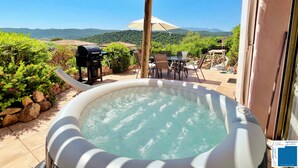 A hot tub with a wooden pergola overhead, a barbecue grill, and a table with chairs.