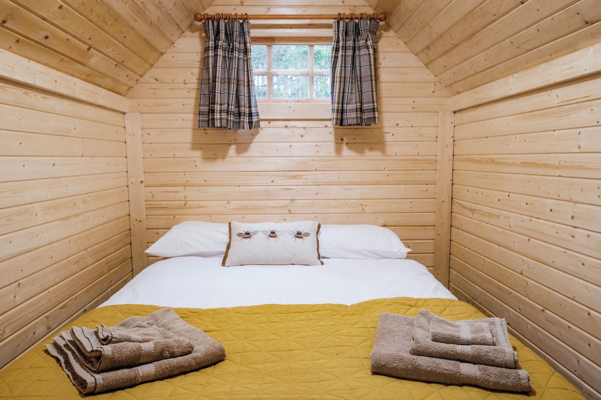 Une chambre de style cabane en bois, avec un lit, une fenêtre ornée de rideaux à carreaux et des serviettes sur le lit.