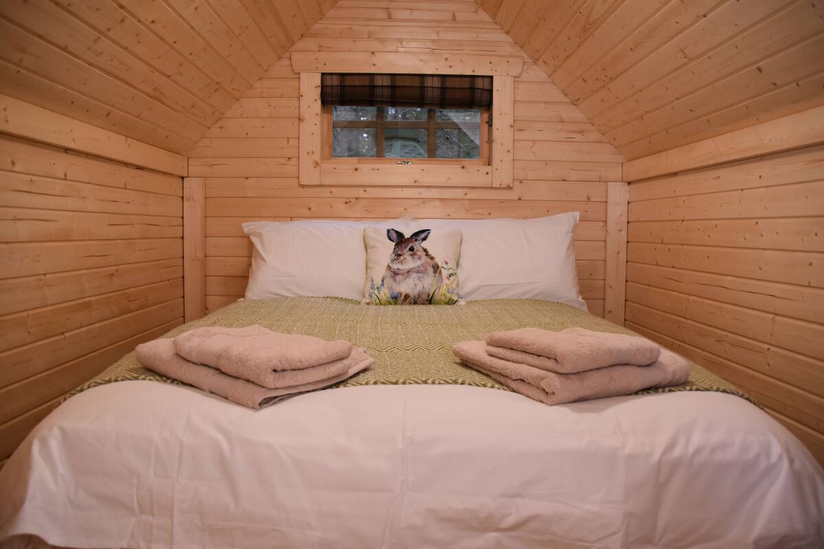 Une chambre confortable, aménagée dans un chalet en bois, avec un lit, des oreillers et une fenêtre.