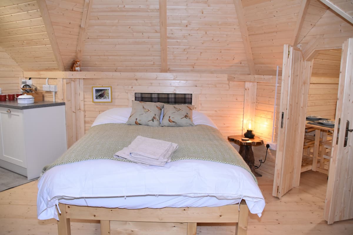 Une chambre dans une cabane en bois, comprenant un lit, une table de chevet et une petite kitchenette.