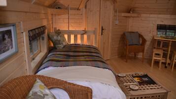 A cozy wooden cabin room with a bed, a chair, a small table, and a framed picture on the wall.