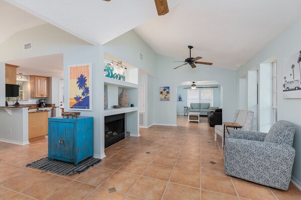 A spacious living area with a fireplace, a blue cabinet, and a sofa. There is a kitchen area with wooden cabinets and a countertop.