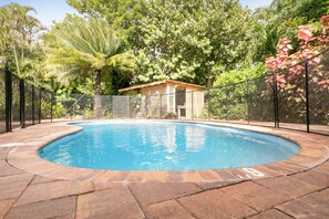 A swimming pool with a curved edge, surrounded by a stone deck and a black fence. - Beachside OASIS - Private Pool - Steps to private beach & restaurants (Melbourne Beach)