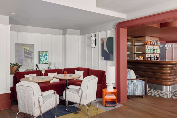 Un área de estar moderna con un sofá rojo, dos sillones, una mesa redonda y una barra con estantes llenos de botellas.