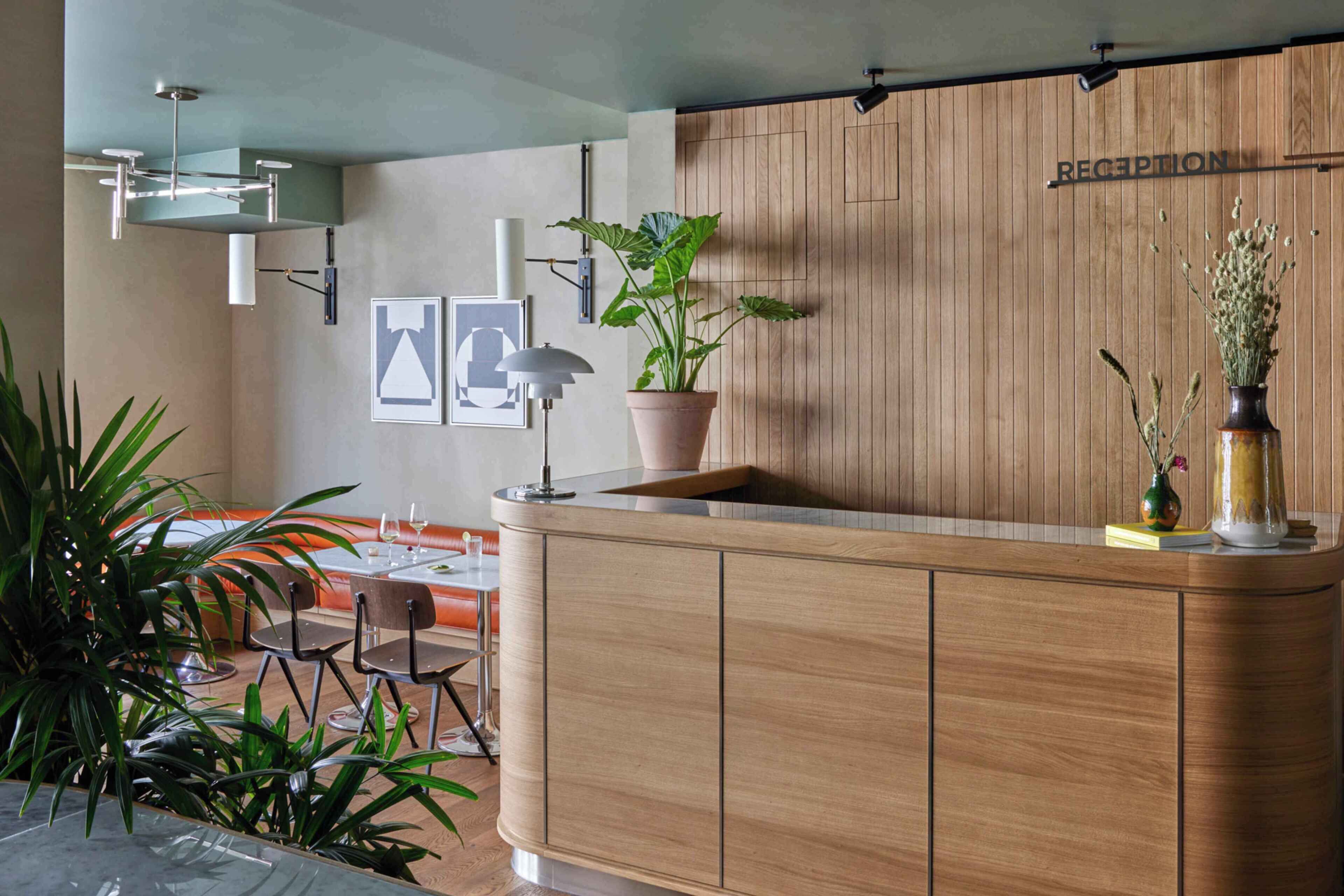 A reception desk with a wooden finish, a potted plant, and a reception sign.