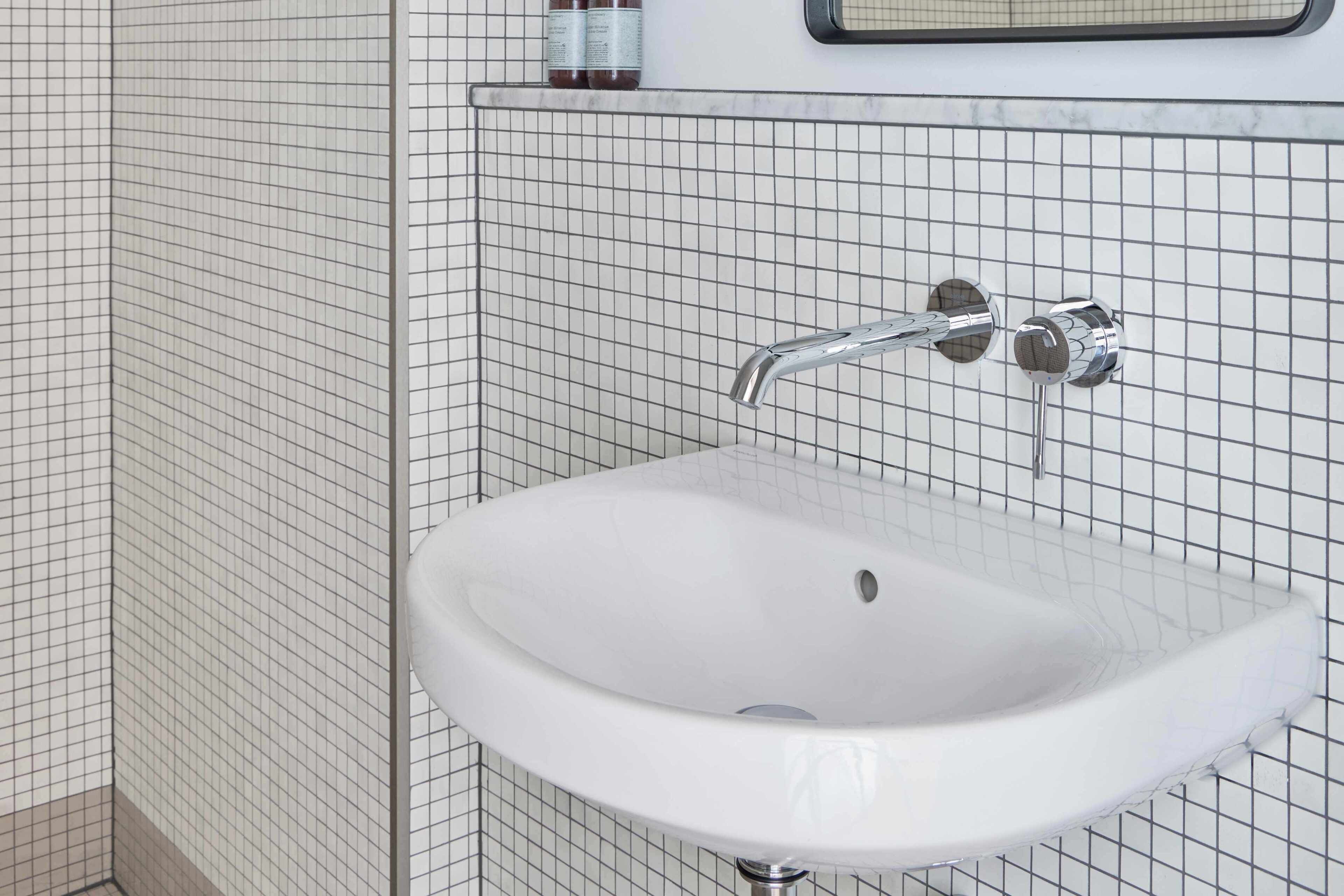 A bathroom with a white sink, chrome faucet, and tiled walls.