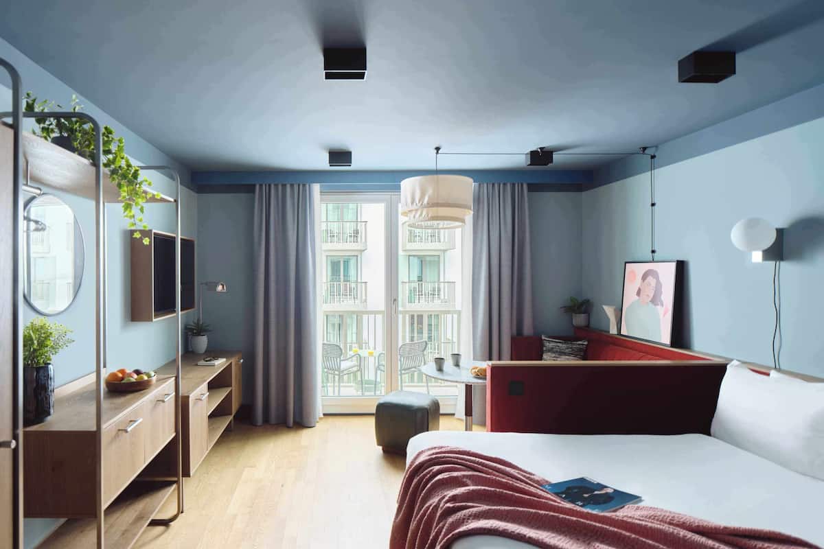 A modern bedroom with a bed, bedside table, dresser, and a balcony view.