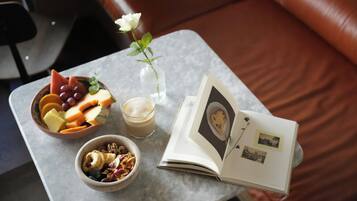 A table with a bowl of fruit, a glass of beverage, a bowl of cereal, a vase with a flower, and an open book with photos.