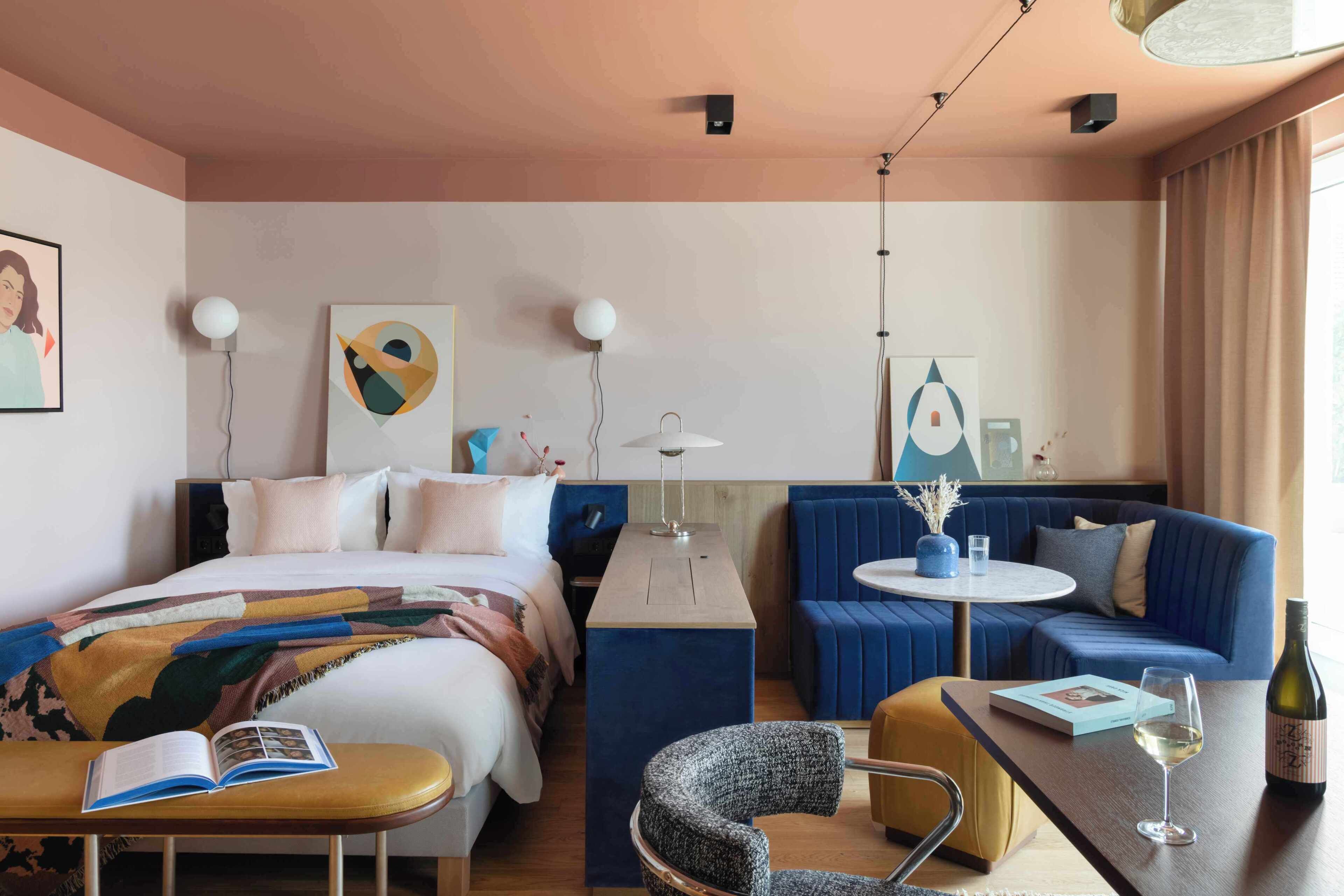 Una habitación de hotel con cama, sofá, una mesita, una silla y una botella de vino.