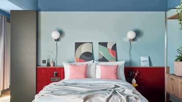 A modern bedroom with a bed, bedside tables, wall art, and a red accent wall.