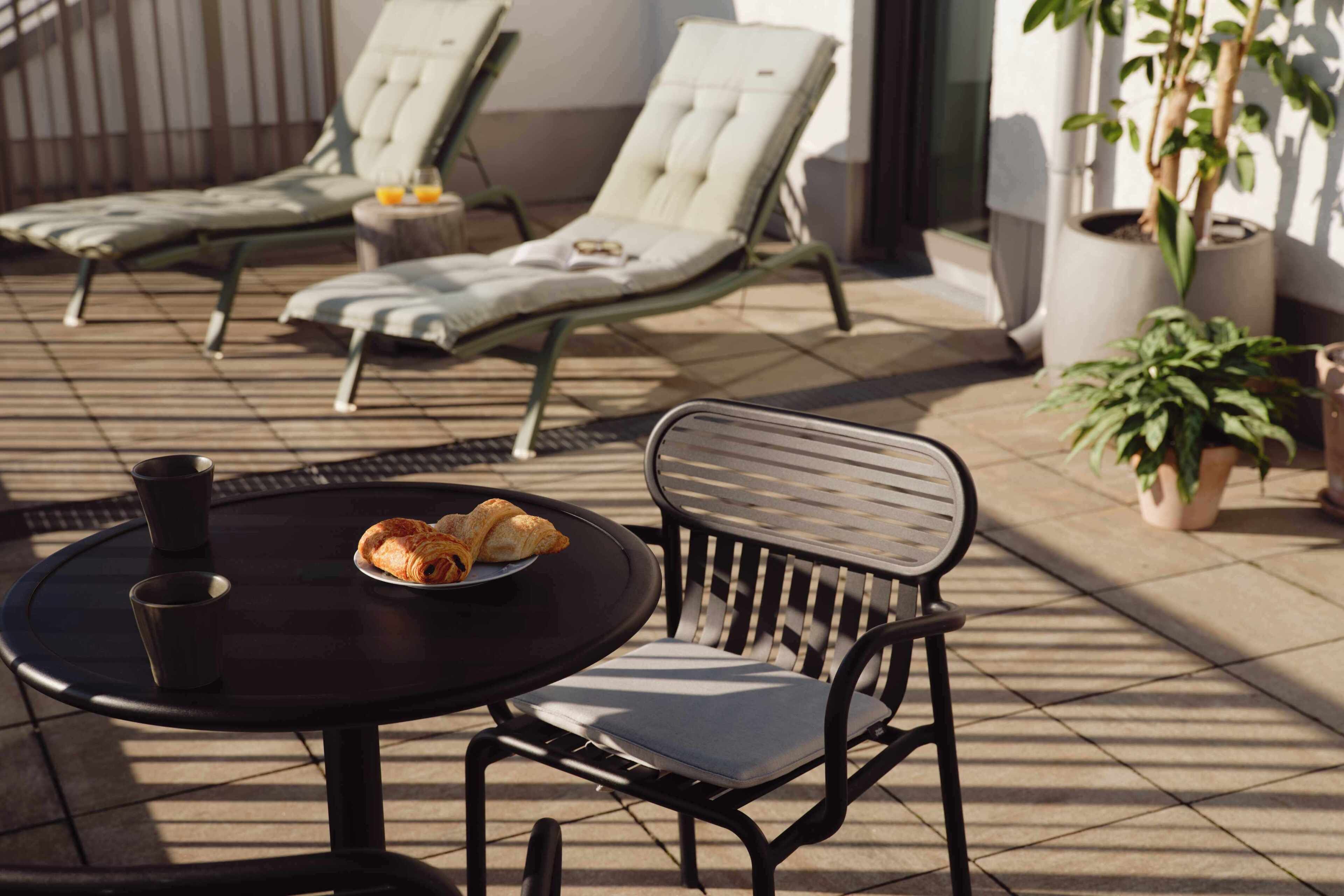 A sunlit outdoor seating area with a table, chairs, and a potted plant.