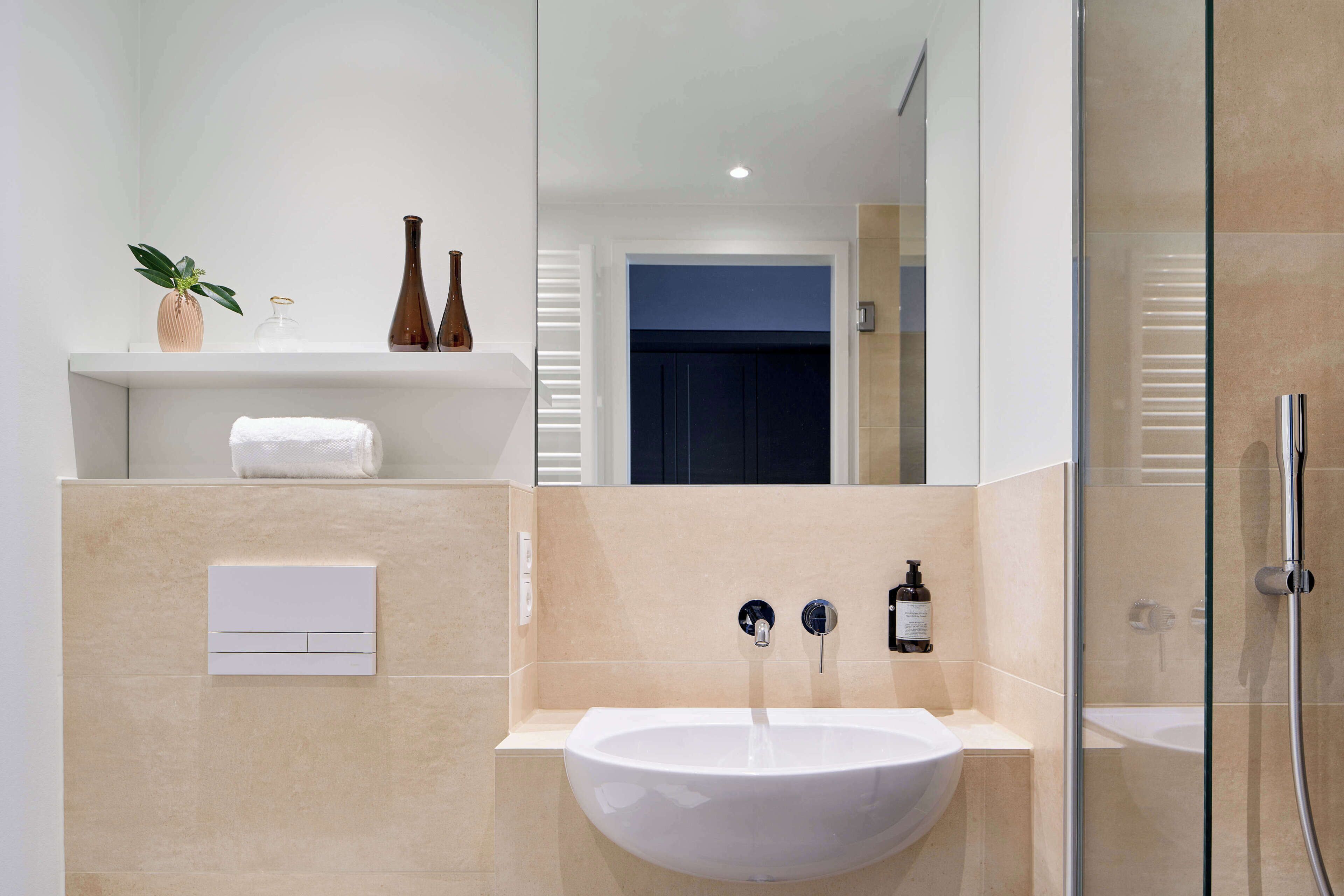 A modern bathroom with a white sink, a mirror, a towel rack, and a shower enclosure.