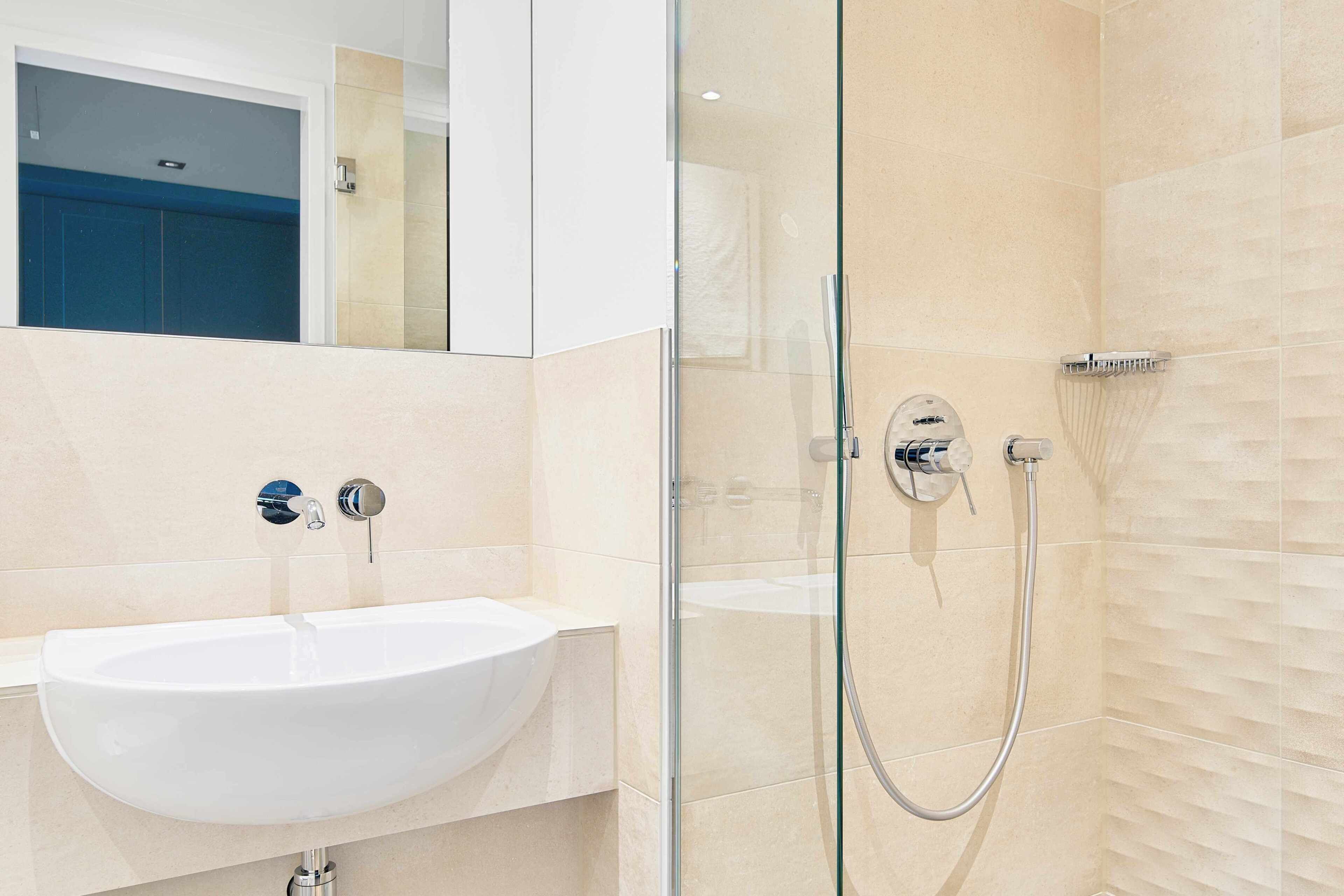 Ein modernes Badezimmer mit einem weißen Waschbecken, einer Duschkabine aus Glas und beige gefliesten Wänden.