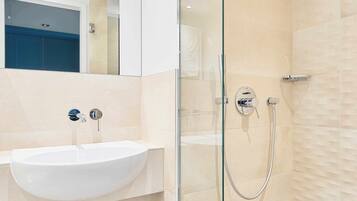 Ein modernes Badezimmer mit einem weißen Waschbecken, einer Duschkabine aus Glas und beige gefliesten Wänden.