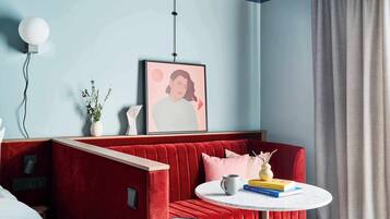 Quarto moderno com sofá de veludo vermelho, uma mesa redonda com livros, uma obra de arte emoldurada na parede e uma planta em vaso.