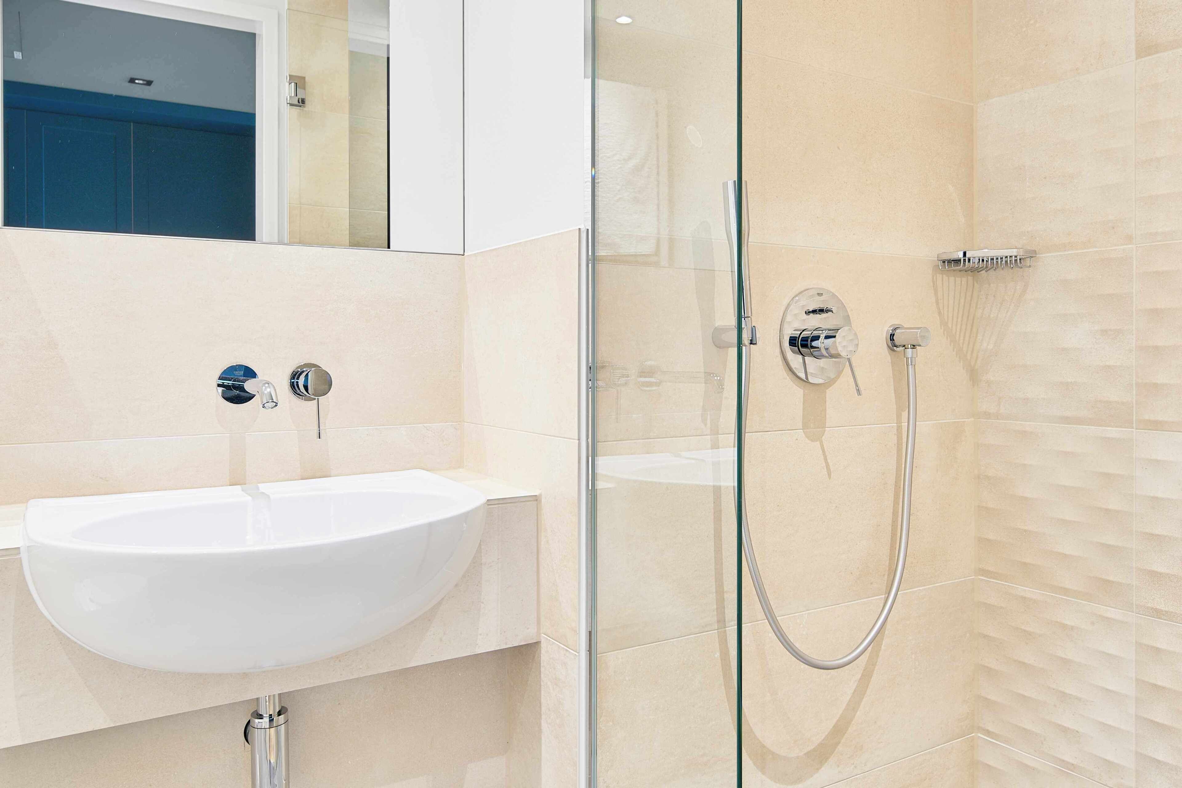 Une salle de bain moderne avec une douche à parois de verre, un lavabo blanc et des murs recouverts de carreaux beiges.