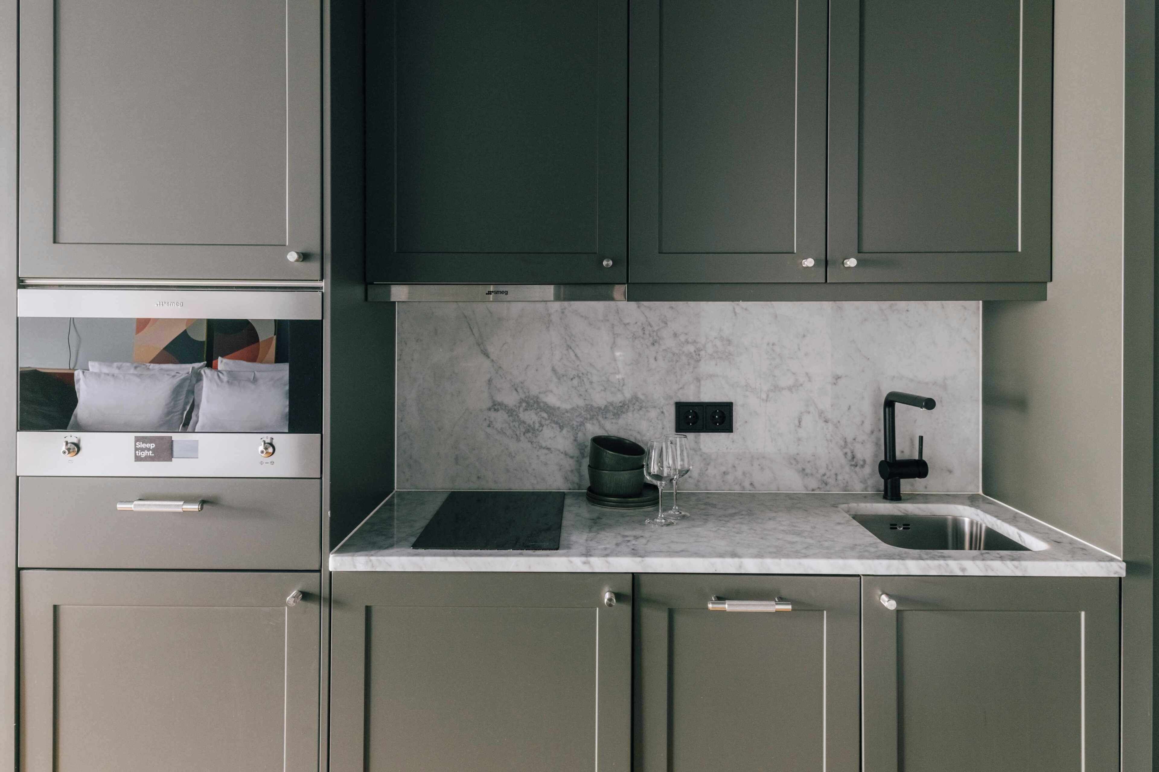 A modern kitchen with grey cabinets, a marble countertop, a black faucet, and a wine glass.