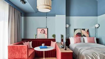 Une chambre d’hôtel moderne avec un canapé rouge, un lit, une table ronde et un grand tableau accroché au mur.