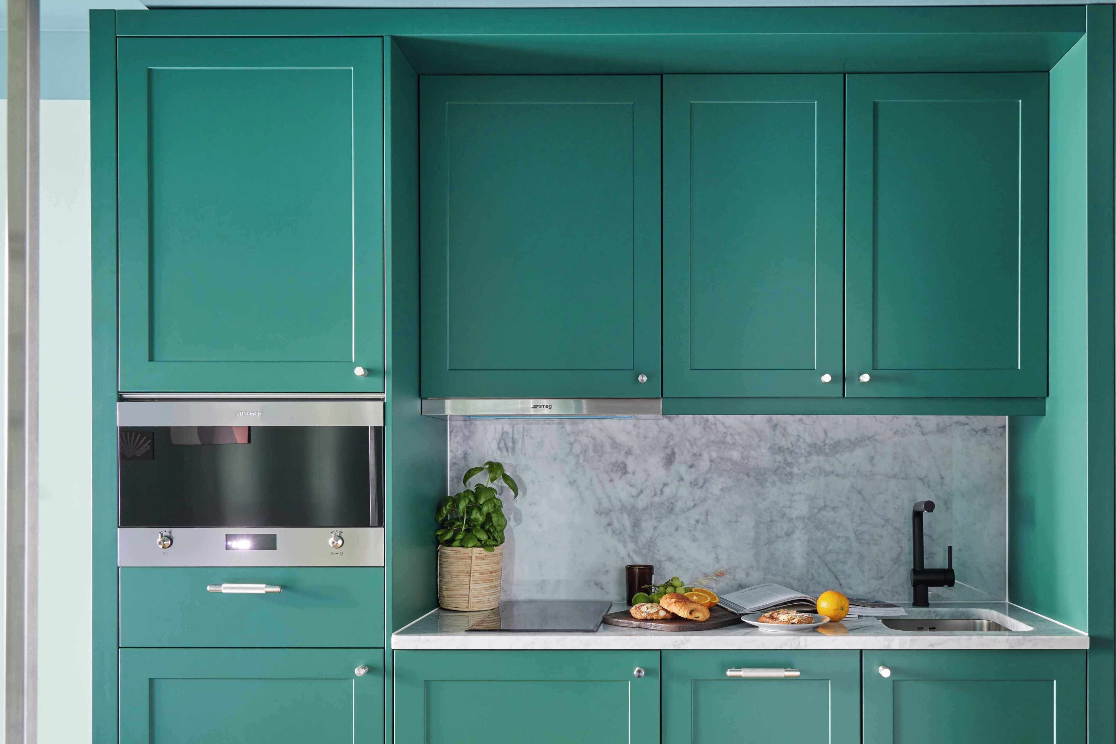 A kitchen with teal cabinets, a stainless steel oven, a marble backsplash, and a sink.