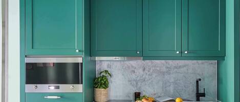 A kitchen with teal cabinets, a stainless steel oven, a marble backsplash, and a sink.
