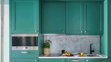 A kitchen with teal cabinets, a stainless steel oven, a marble backsplash, and a sink with a black faucet.