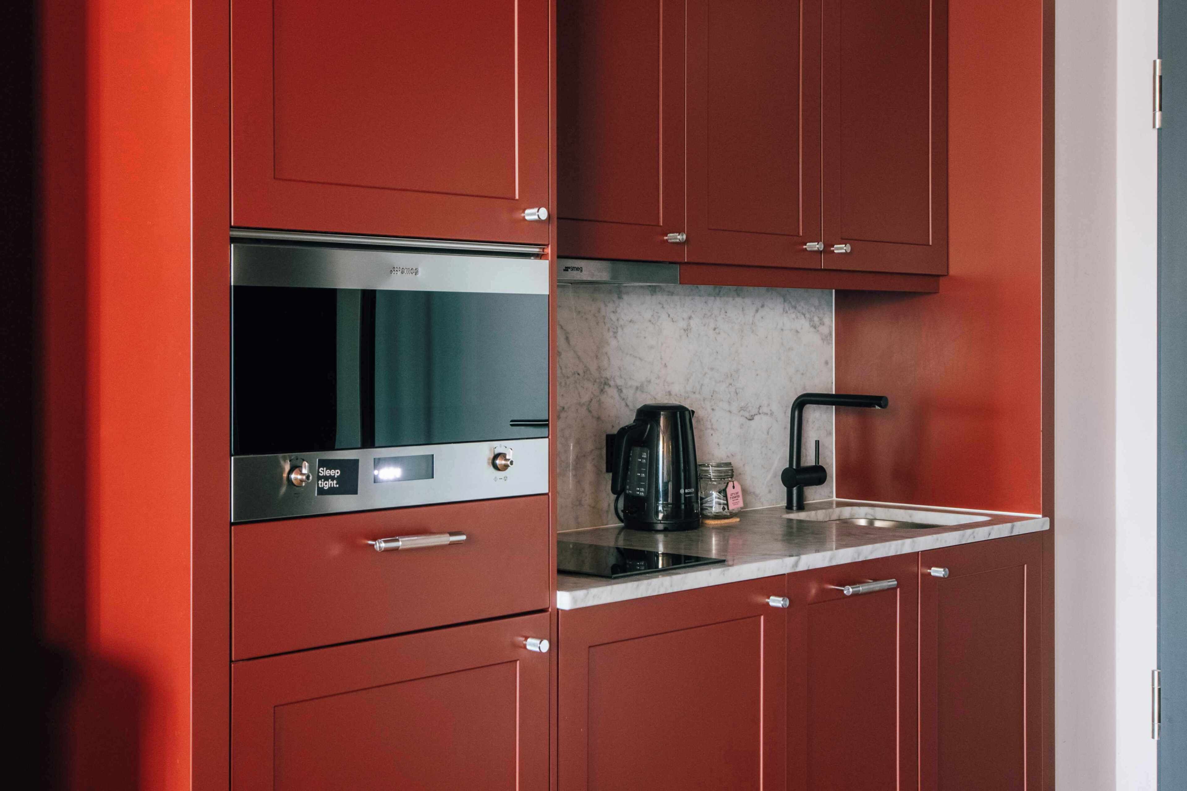 A kitchen with red cabinets, a stainless steel range hood, a coffee maker, and a marble countertop.