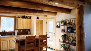 A rustic kitchen with wooden cabinets, a dining table with chairs, and a shelf with decorative items. - Private Hot Tub in the Aspens - Steam Shower, Log Fireplace, Mtn Views (Alma)