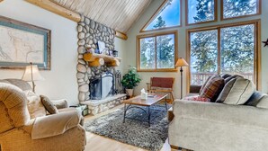 A cozy living room with a stone fireplace, large windows, and a high ceiling. - Private Hot Tub in the Aspens - Steam Shower, Log Fireplace, Mtn Views (Alma)