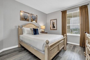 A bedroom with a wooden bed, a nightstand, a lamp, and artwork on the walls.