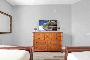 A bedroom with a wooden dresser, a painting of a tropical scene, and two wooden beds.