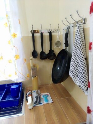 A kitchen with hanging pots and pans, a blue plastic container, and a grater on the counter. - Remarkable 1-bed Guest House in Bungoma (Bungoma)