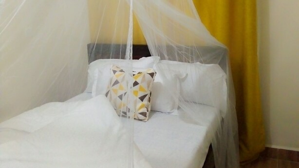 Un letto con tenda bianca e tendaggio giallo.