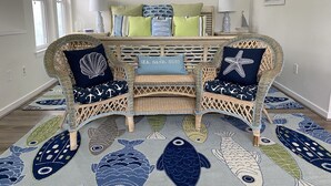Une pièce avec des fauteuils en osier, un canapé et un tapis orné de motifs de poissons.