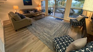 Un salon spacieux avec une grande fenêtre, un ensemble de canapés, une table basse et un pouf à motifs.