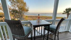 Ett trädäck med två fåtöljer i rotting och ett bord, med utsikt över en sjö eller ett hav och en strand.