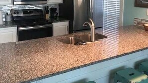 Cocina con gabinetes blancos, electrodomésticos de acero inoxidable, encimera de granito y taburetes de bar color turquesa.