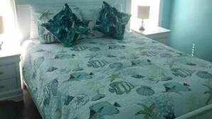 Un dormitorio con una cama, dos mesitas de noche, una ventana con persianas y un cuadro en la pared.