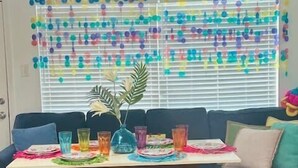 Un salón con sofá, una mesa de comedor con cristalería de colores y una pared decorativa con adornos colgantes.