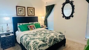 Un dormitorio con cama, mesita de noche, ventilador de techo, espejo y ventana con cortinas.
