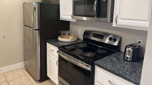 Una cocina con alacenas blancas, un refrigerador de acero inoxidable, un microondas, una estufa y un tostador.