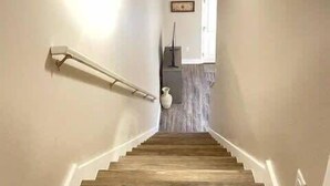 Una escalera de madera con barandilla que conduce a una habitación con una puerta blanca y un jarrón sobre un pedestal.