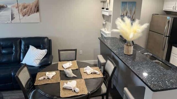 Una cocina moderna con encimera de granito, una zona de comedor con una mesa redonda y sillas, y un sofá de cuero negro.