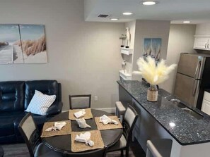A modern kitchen with a granite countertop, a dining area with a round table and chairs, and a black leather sofa.