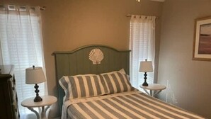 Un lit avec une couvre-lit à rayures, deux tables de chevet avec des lampes et un coquillage décoratif sur la tête de lit.