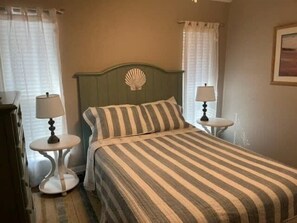 A bed with a striped bedspread, two bedside tables with lamps, and a decorative shell on the headboard. - Island Dunes Condo's-#1109-One Block from Beach. (Port Aransas)