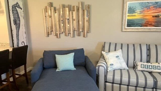 Un salon comprenant un canapé, un fauteuil à rayures, une œuvre d’art murale en bois et un tableau encadré.