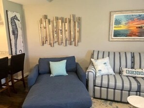 A living room with a sofa, a striped armchair, a wooden wall art piece, and a framed painting.