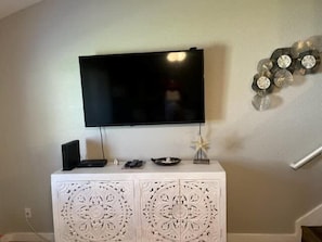 Un televisor de pantalla plana montado en una pared sobre un mueble blanco con detalles tallados.